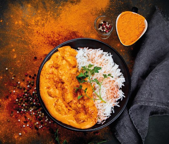 Traditional Punjabi Street Food in Northampton Chicken curry and rice in a black bowl with turmeric splashed on the table underneath