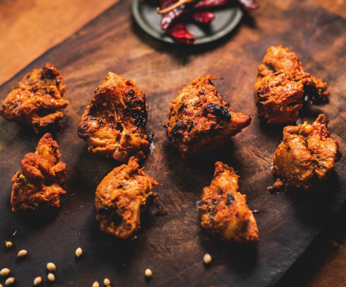 Amazing Punjabi Street Food Restaurant, Wellingborough Road, Norhtampton Cooked chicken marinated in spices laying on a wooden board, garnished with dried chilli